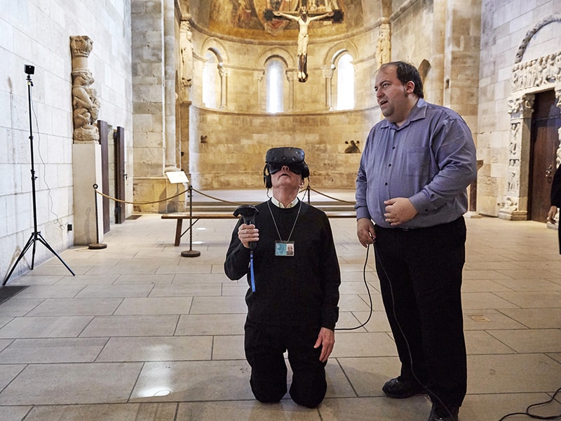 The Rev. Xavier Seubert, left, of the Friary of St. Francis of Assisi in Manhattan explores the interior of an intricately carved prayer bead using a VR headset, guided by Joseph Ellsworth of the Canadian Film Center, on April 3, 2017. The exhibit "Small Wonders: The VR Experience" at The Met Cloisters Museum in New York City is an immersive experience that takes museum patrons inside a miniature, wooden prayer bead using micro-CT imaging technology and a VR headset. RNS photo by Steve Remich