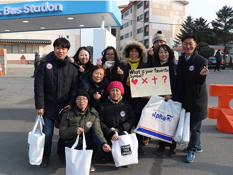 Volunteers with Cru (Campus Crusade for Christ) stand at the bus station by Olympic Park,  asking spectators their favorite symbol, and using it as a connection to start a conversation on religion, on Feb. 8, 2018, in South Korea. (RNS photo: Madeline C. Mulkey) 