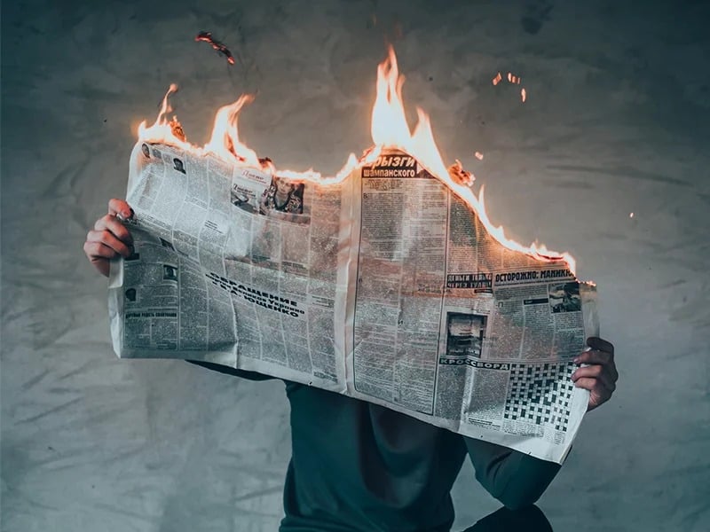 A photo illustration of a newspaper in flames. Photo by Elijah O’Donell via Unsplash/Creative Commons
