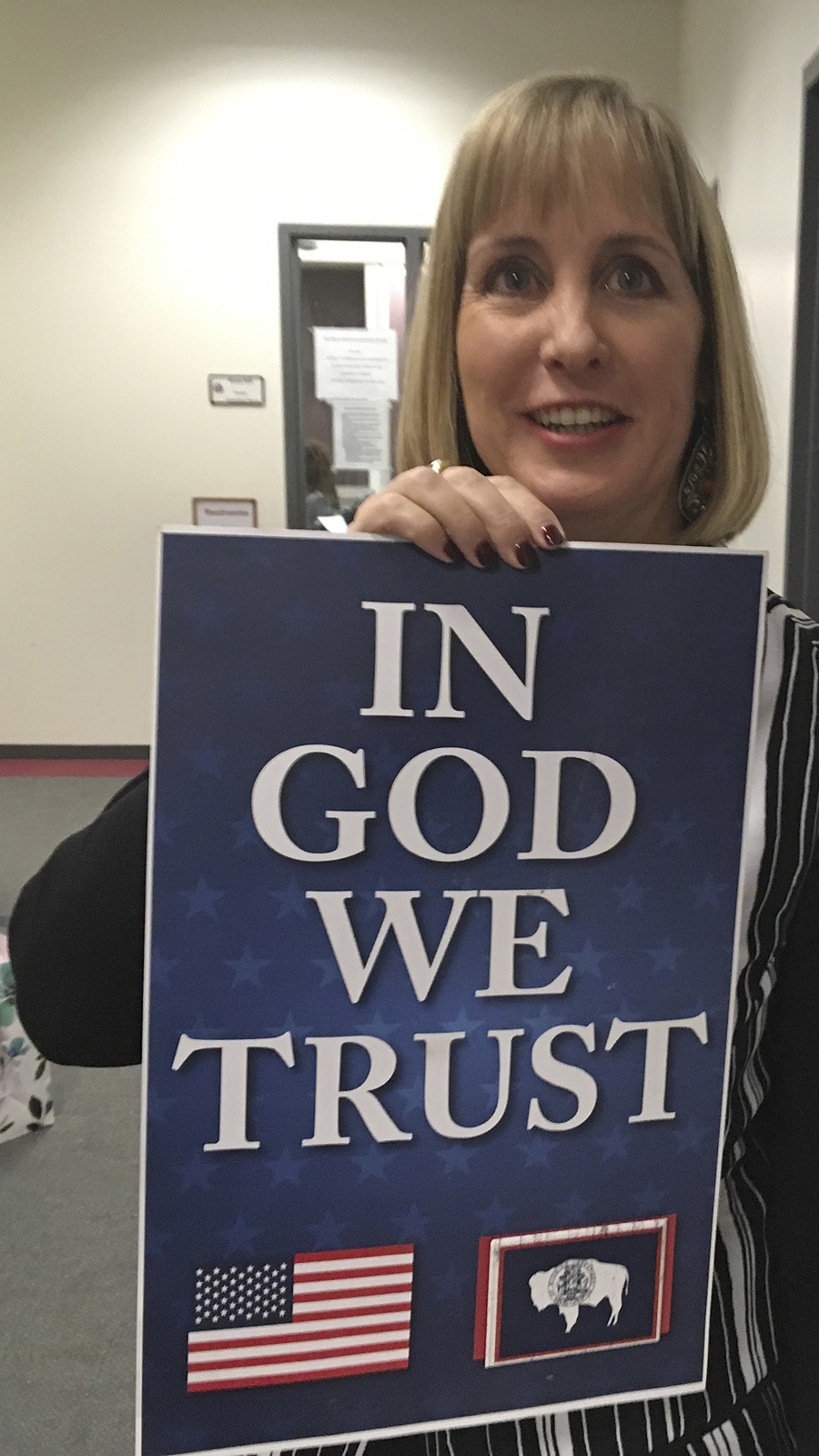 Wyoming State Rep. Cheri Steinmetz,R-Lingle, on March 6, 2018, shows an example of an “In God We Trust” placard in Cheyenne, Wyo. Steinmetz sponsored a bill that would allow people to donate such placards for display in prominent places in state buildings and schools. The measure died in the state Senate. (AP Photo by Bob Moen)