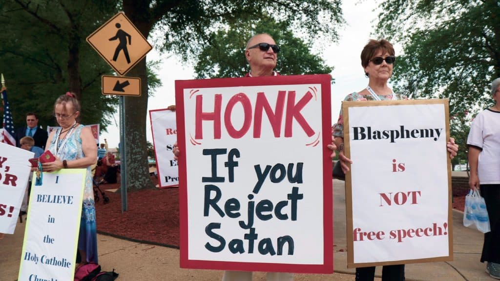Protesters hold signs against The Satanic Temple